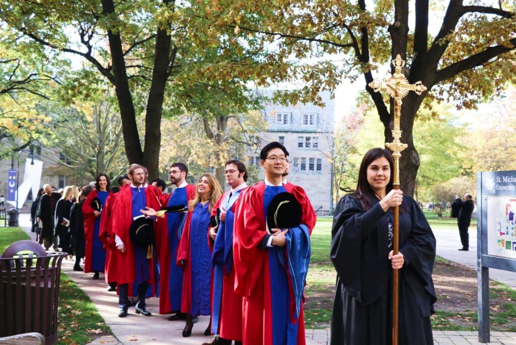 Students in graduation gowns being led in procession on campus